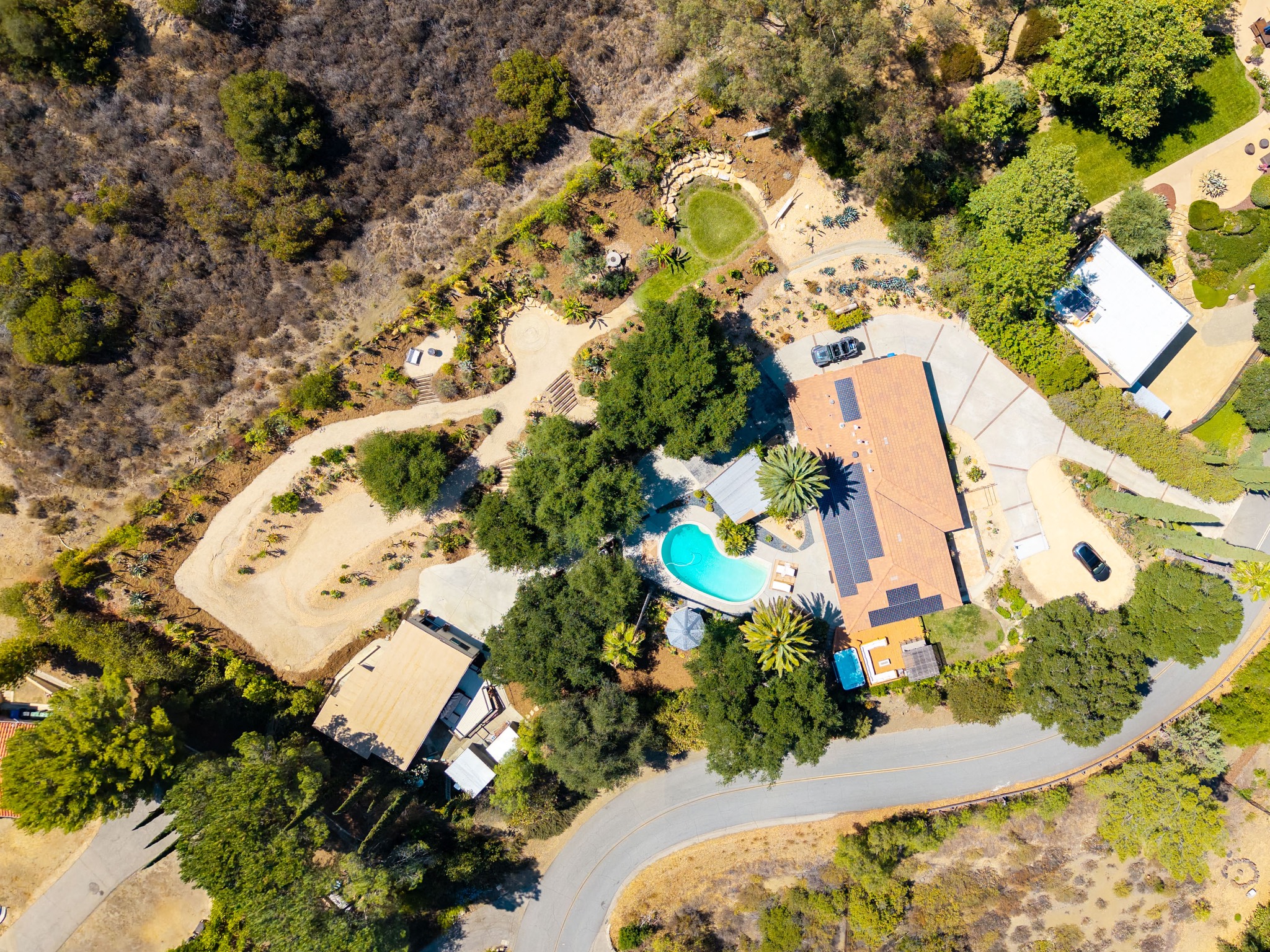 Hero drone view of the full DreamsAwake estate: house, saltwater pool, circular lawn, wandering garden paths, and the studio in the Calabasas canyon