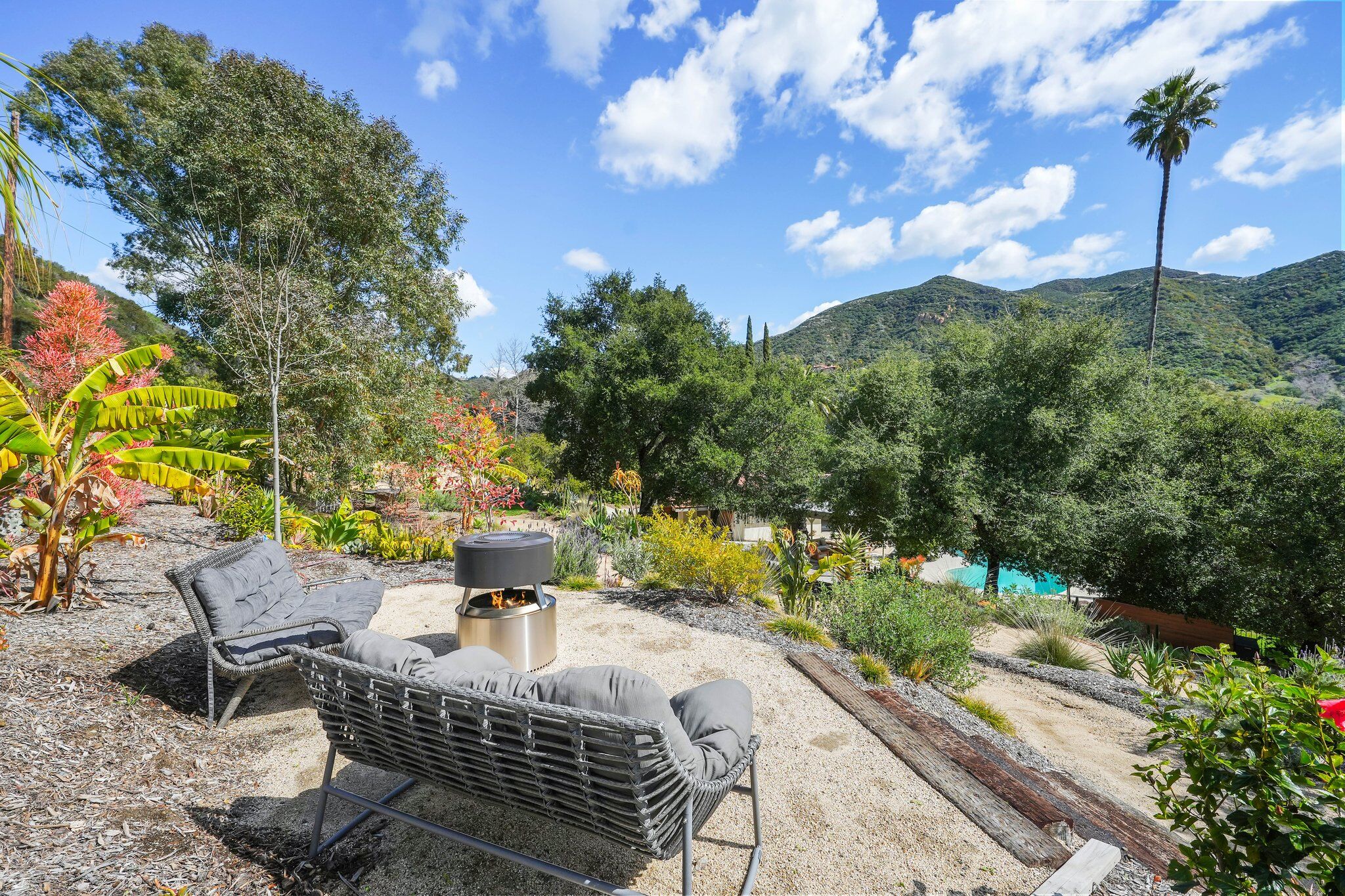 Grey loungers around a fire pit on a gravel terrace with the pool and canyon ridgelines below