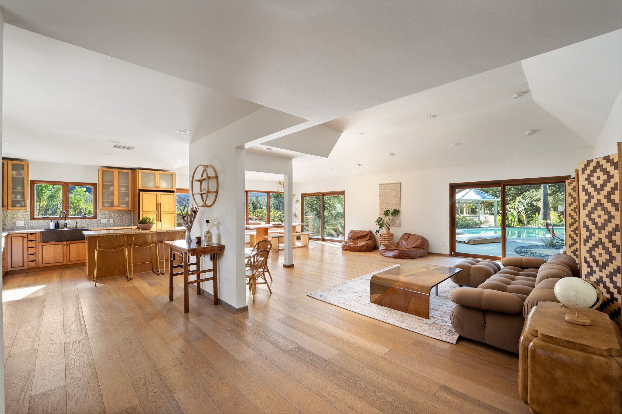 Open-concept great room flowing into the kitchen and dining area, with pool views through walls of glass