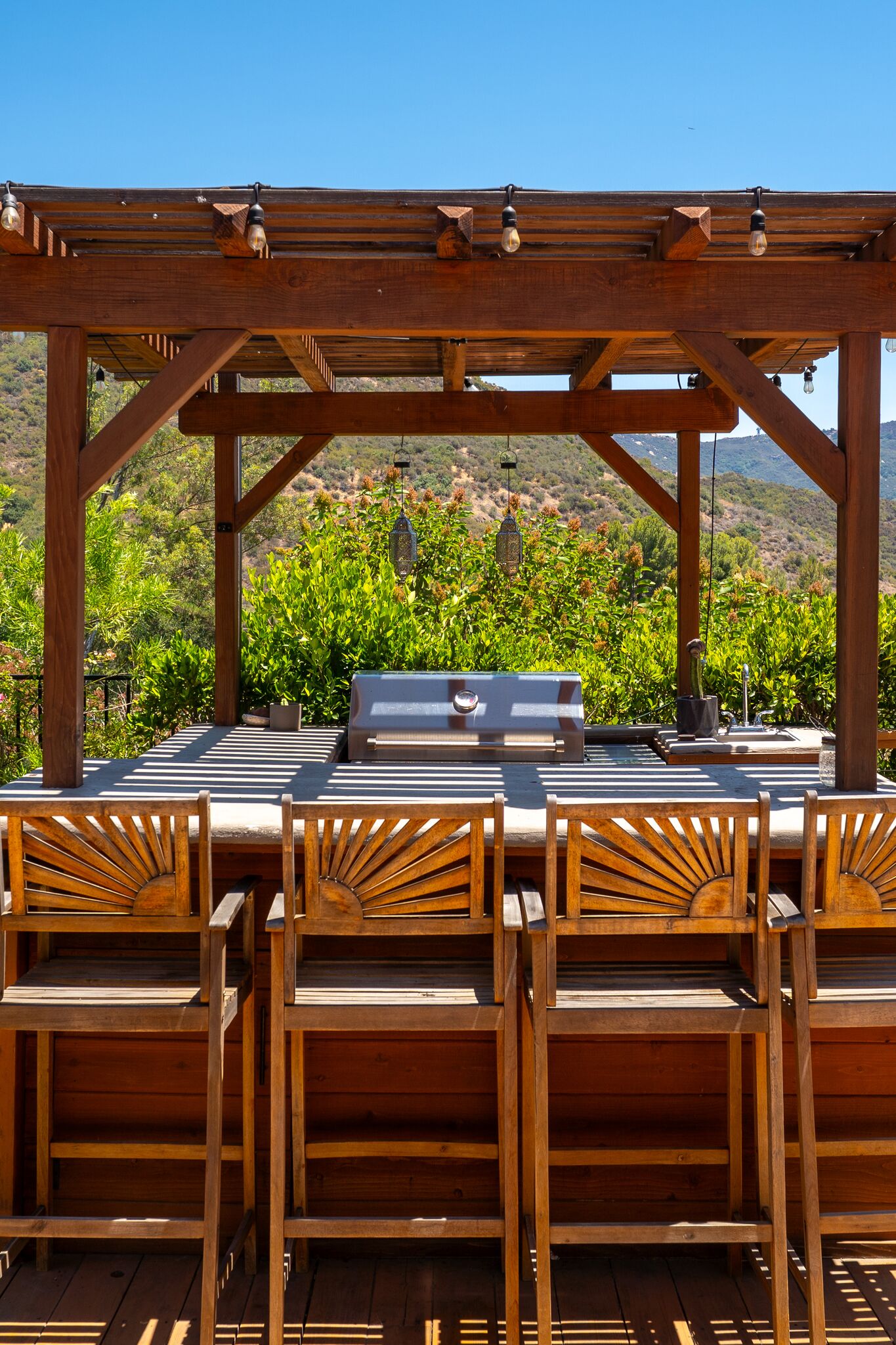 Pergola bar with counter stools beside the swim spa, gazebo and gardens beyond