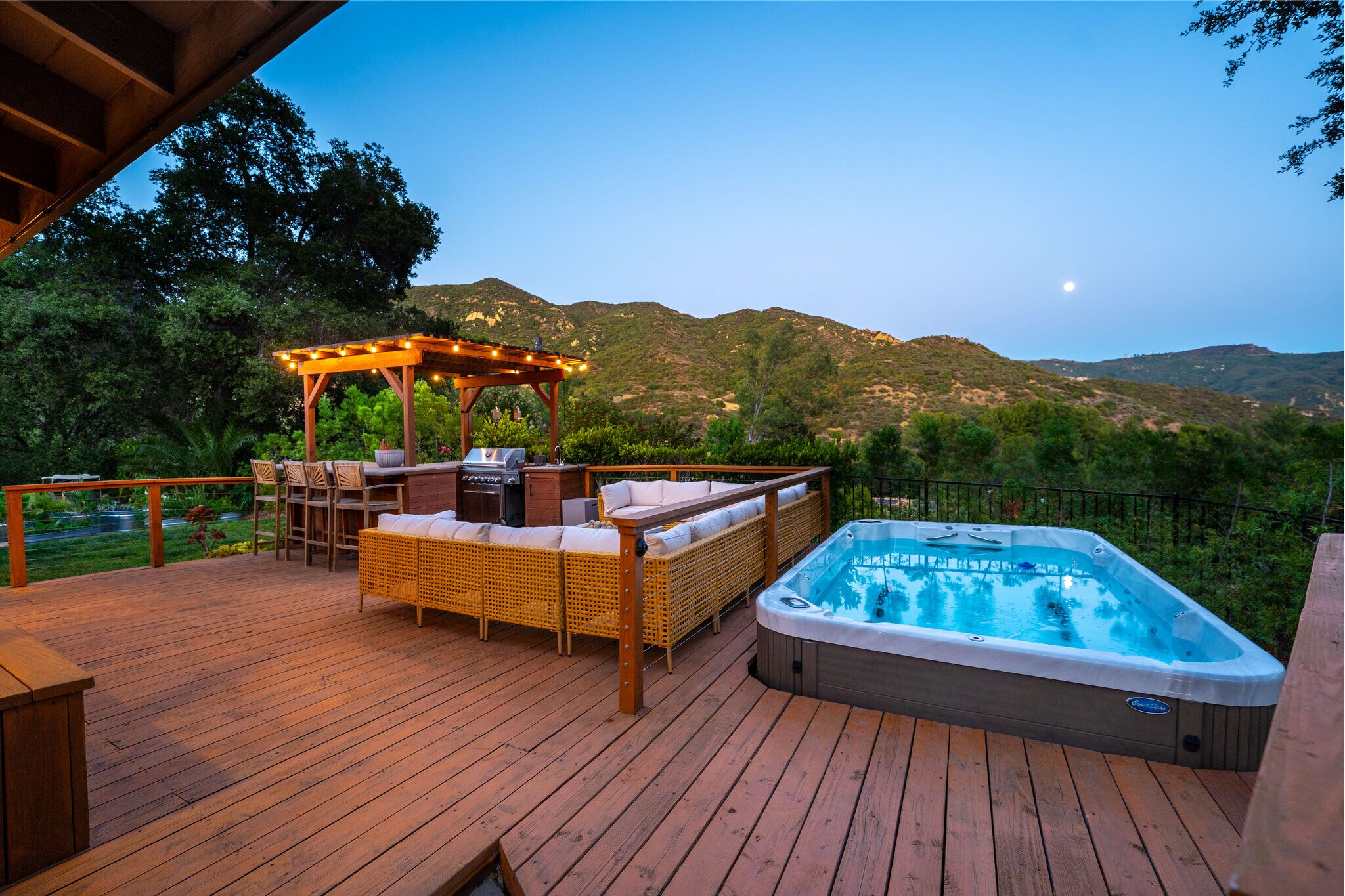 Spa deck at dusk with swim spa, pergola bar with string lights, and canyon mountain views