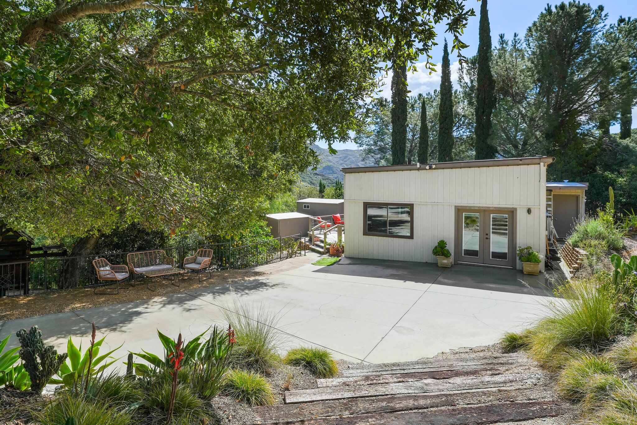 The white studio with glass doors on a wide concrete pad shaded by an old oak